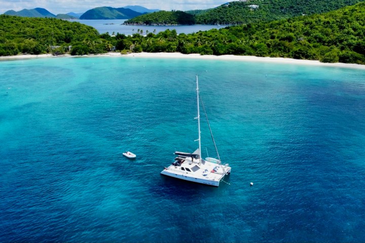 Sailboat anchored in turquoise water near a lush green island.